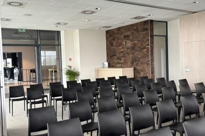 Rangées de chaises noires alignées dans une salle lumineuse avec une table en bois au premier plan.
