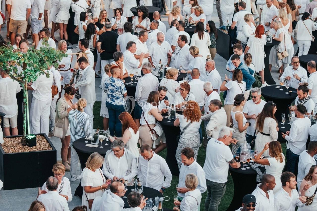 Groupe de personnes en tenue blanche rassemblées autour de tables noires lors d'un événement en plein air.
