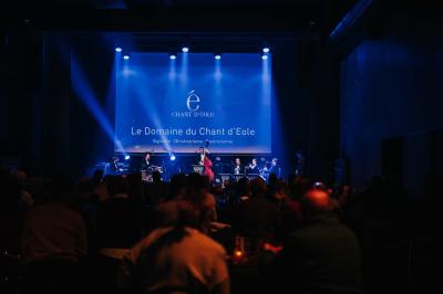 Rangées de chaises noires alignées dans une salle lumineuse avec une table en bois au premier plan.
