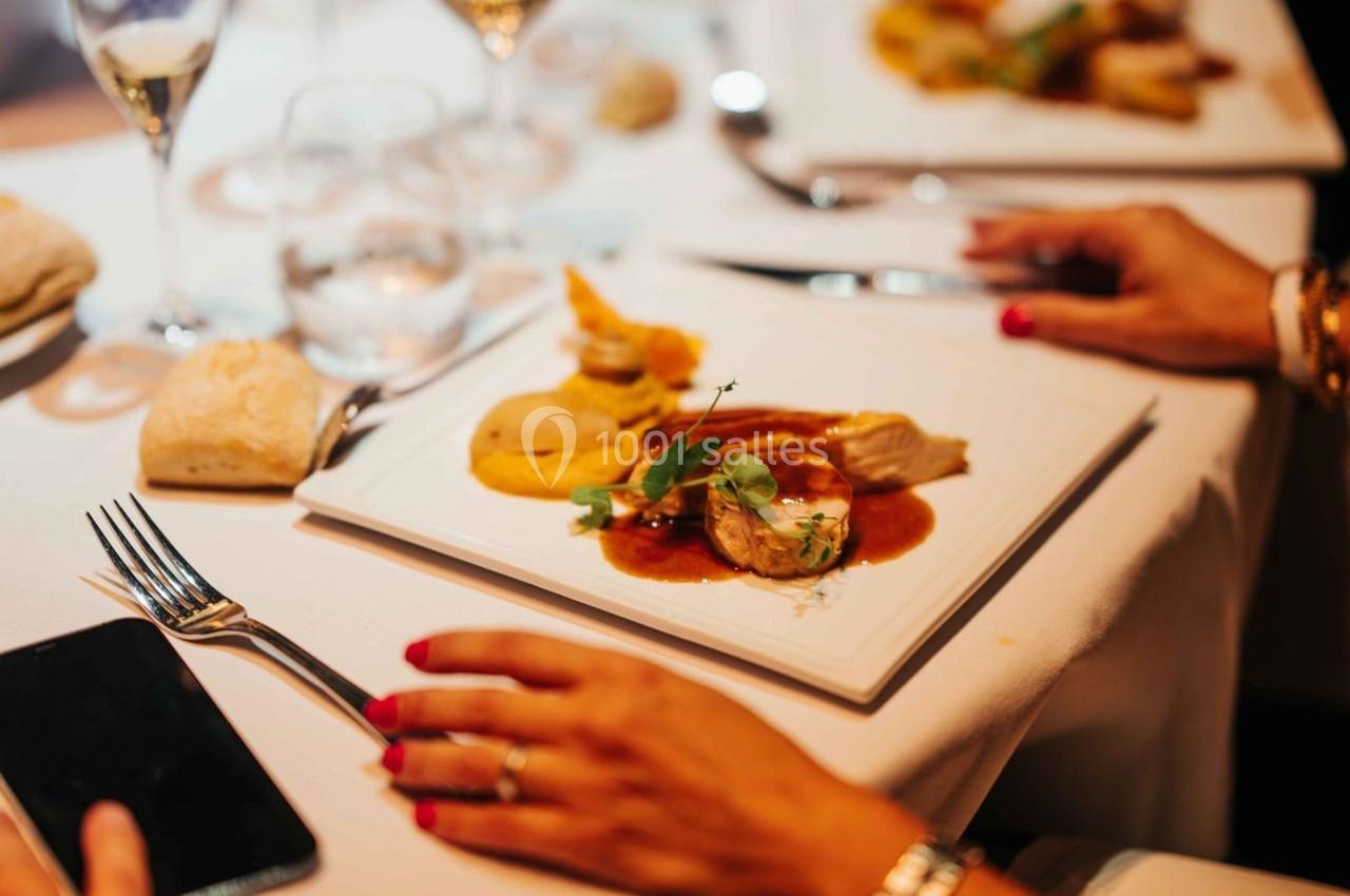 Assiette gastronomique avec viande, purée et sauce, posée sur une table élégamment dressée avec des couverts.
