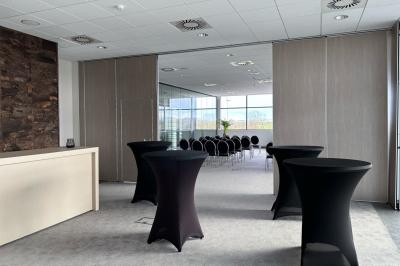 Rangées de chaises noires alignées dans une salle lumineuse avec une table en bois au premier plan.