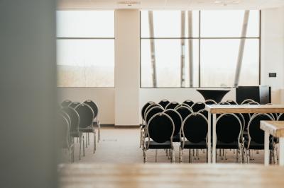 Rangées de chaises noires alignées dans une salle lumineuse avec une table en bois au premier plan.