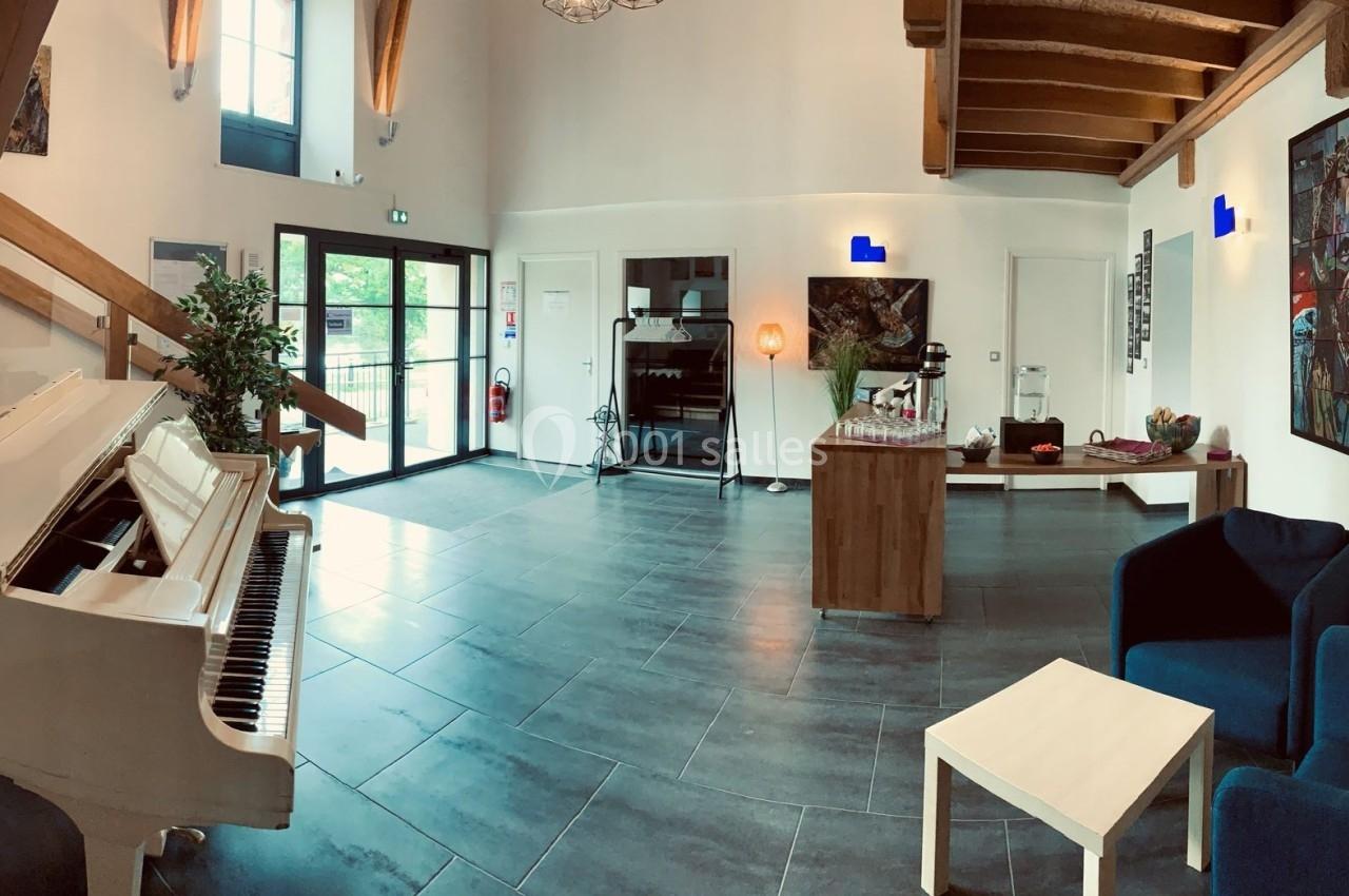 Intérieur lumineux avec un piano blanc, des fauteuils bleus, un escalier en bois et des œuvres d'art accrochées aux murs.