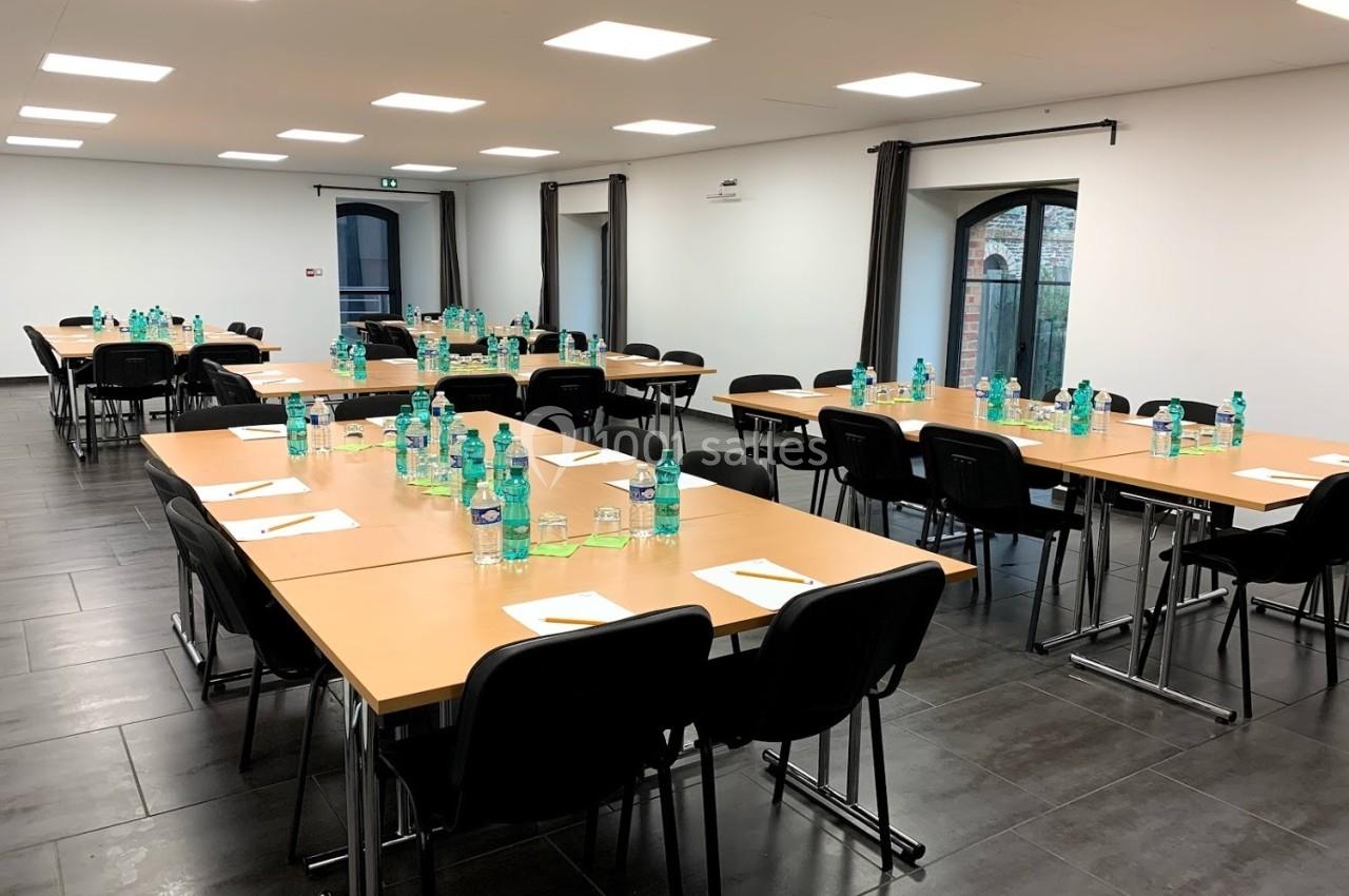 Salle de réunion avec plusieurs tables disposées en U, équipées de bouteilles d'eau, de verres et de blocs-notes.