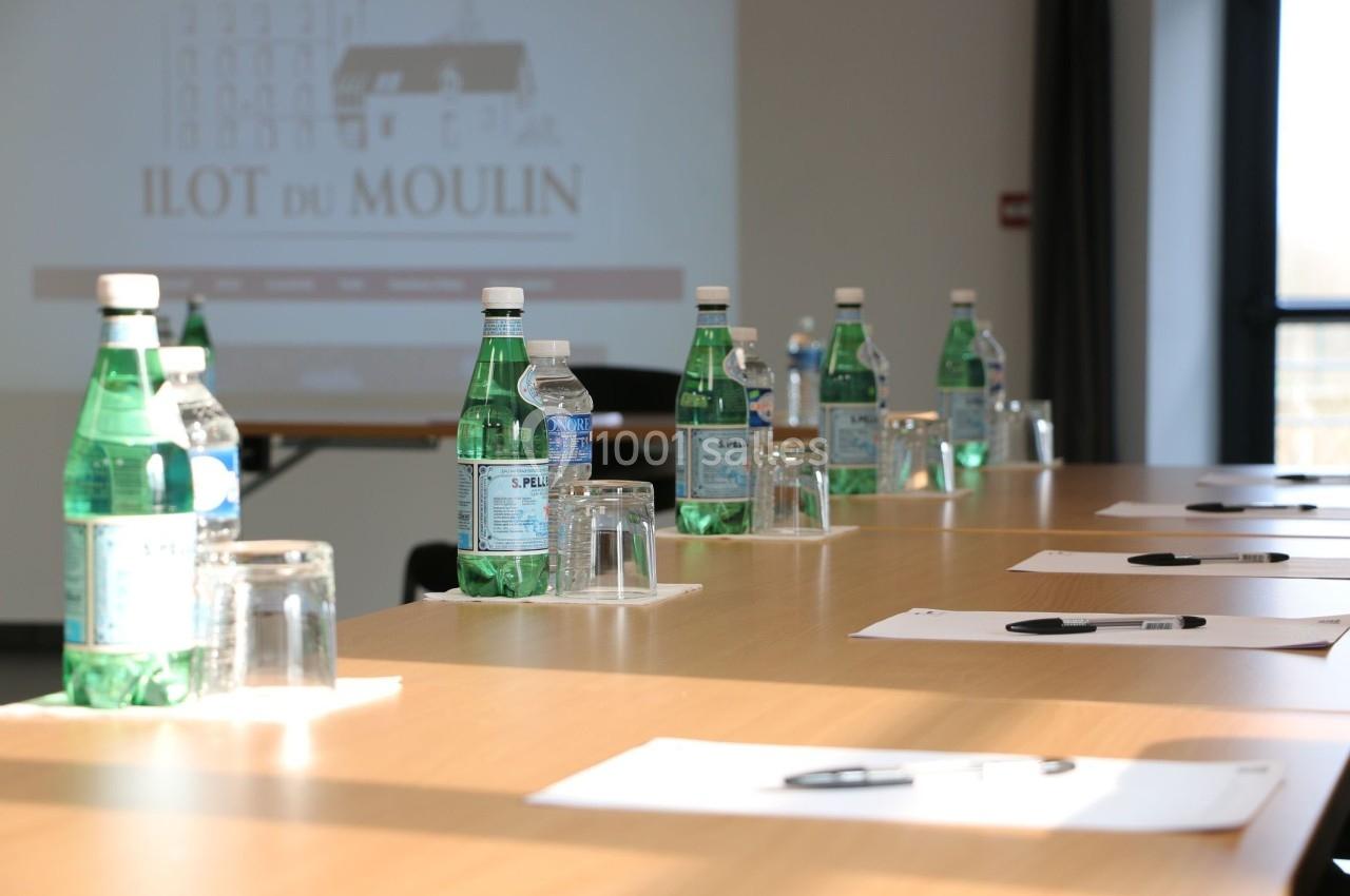 Bouteilles d'eau, verres et documents disposés sur une table de réunion éclairée par la lumière naturelle.