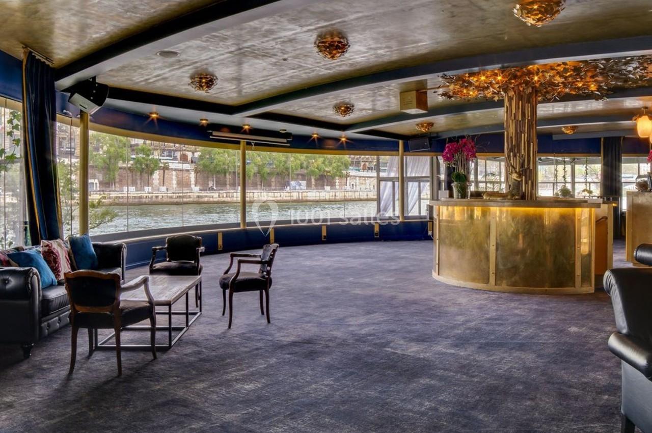 Salle élégante avec grandes baies vitrées, mobilier chic et comptoir doré, offrant une vue sur un canal.