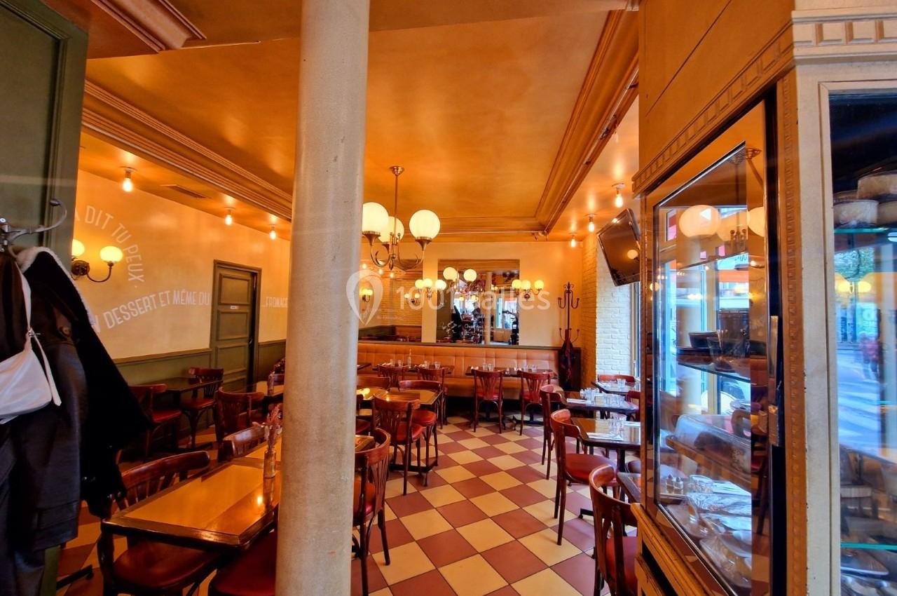 Salle de restaurant avec tables en bois, chaises rouges, éclairage chaleureux et sol à carreaux beige et rouge.