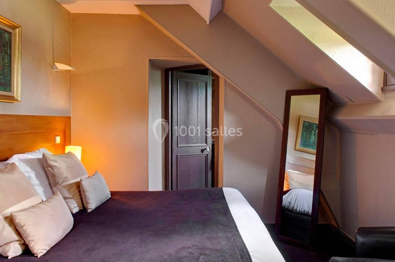 Chambre mansardée avec lit double, miroir sur pied, tableau au mur et lumière naturelle provenant d'une fenêtre.