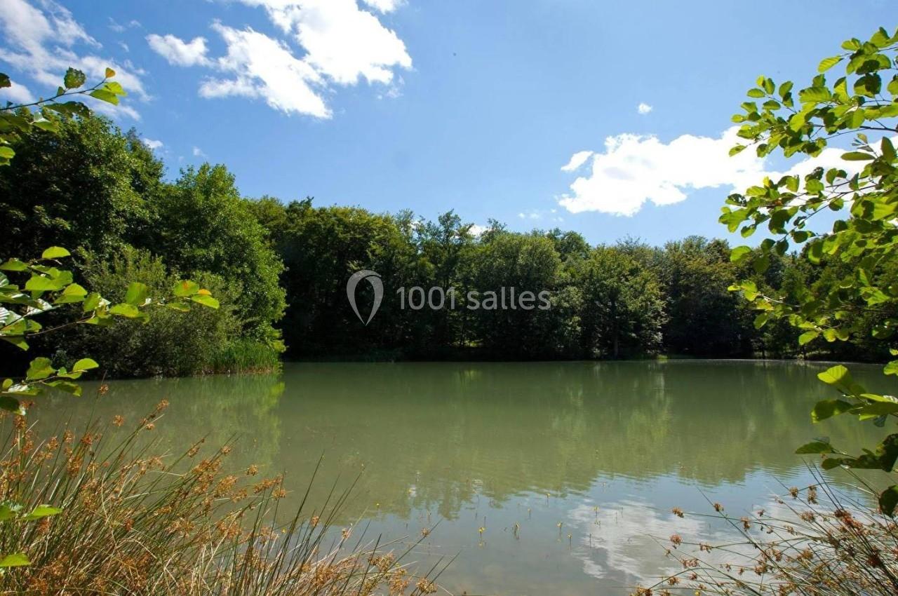 Plan d'eau entouré de végétation dense sous un ciel bleu avec quelques nuages.