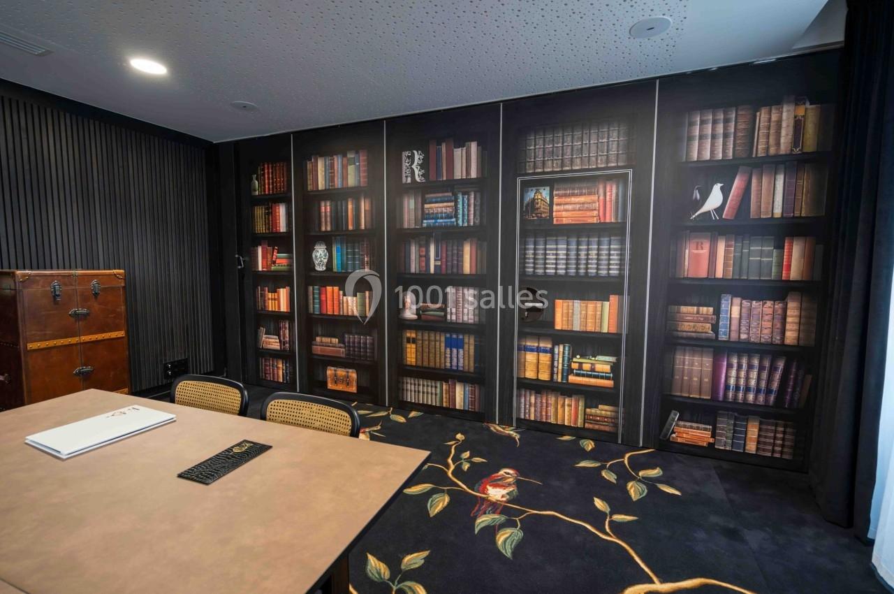 Salle de réunion avec table, chaises et mur décoré d'une fresque représentant une bibliothèque.