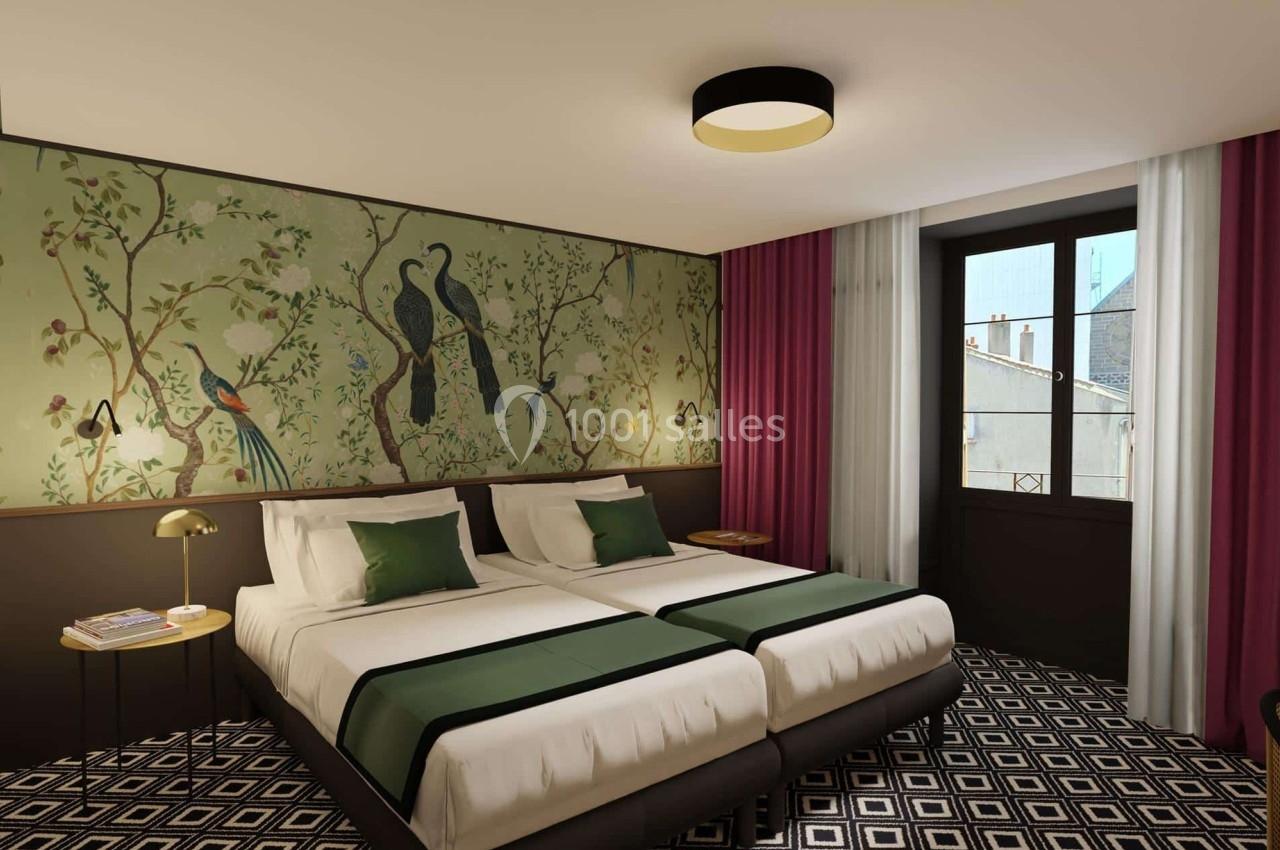Deux lits simples avec linge vert, mur décoré de motifs d'oiseaux, fenêtre donnant sur des bâtiments, sol à motifs…