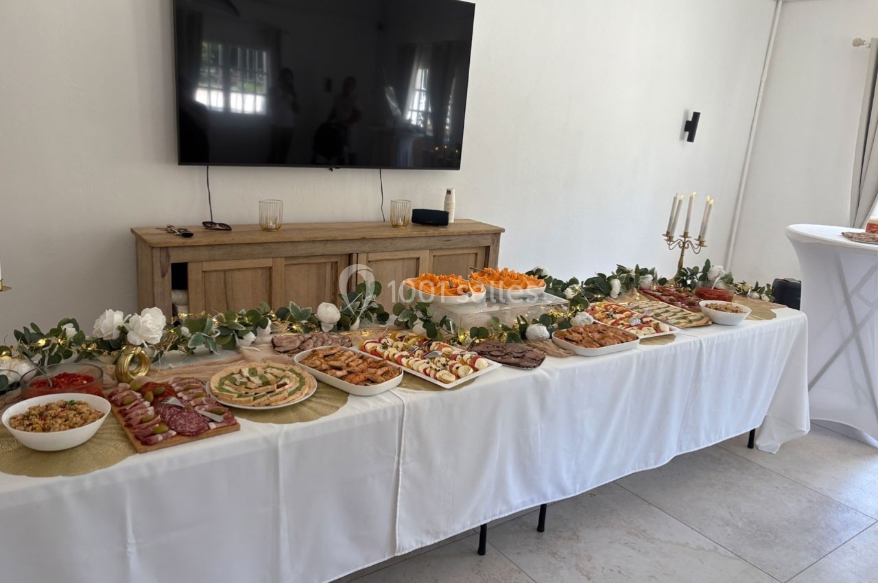Table garnie de divers plats et amuse-bouches, décorée de guirlandes végétales et située dans une pièce lumineuse.