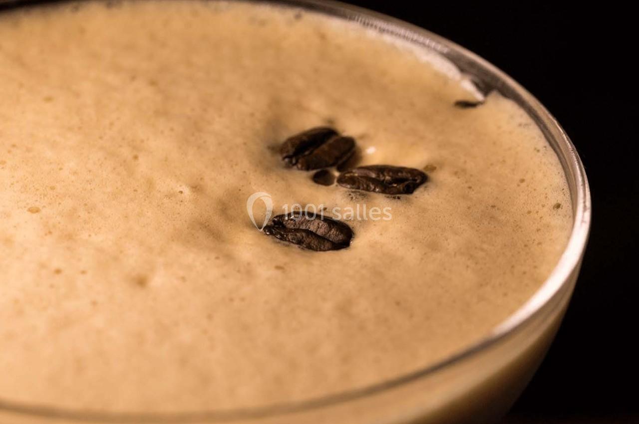 Vue rapprochée d'une mousse de café garnie de grains de café entiers dans un verre transparent.