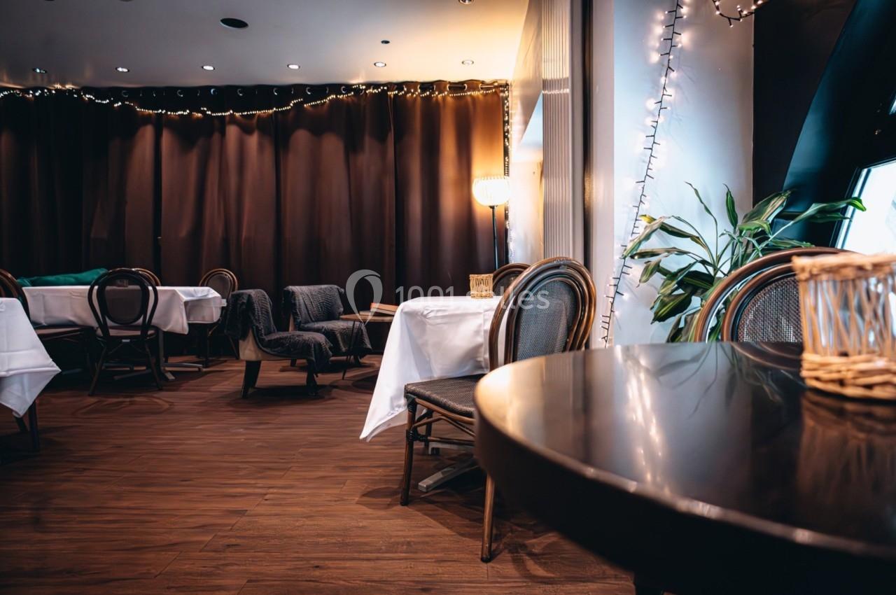 Salle de restaurant avec tables dressées, chaises en bois, éclairage tamisé et guirlandes lumineuses.
