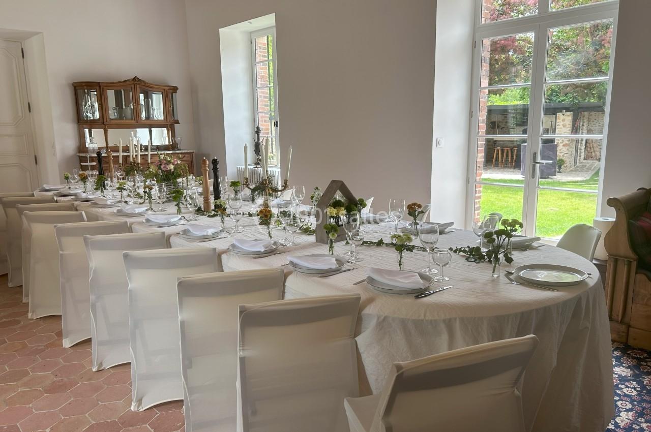 Table dressée pour un repas, avec nappes blanches, vaisselle élégante et décor floral, dans une salle lumineuse.