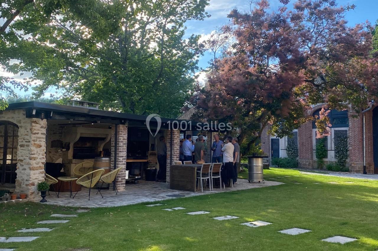 Un groupe de personnes rassemblé près d'une terrasse couverte dans un jardin verdoyant sous un ciel dégagé.