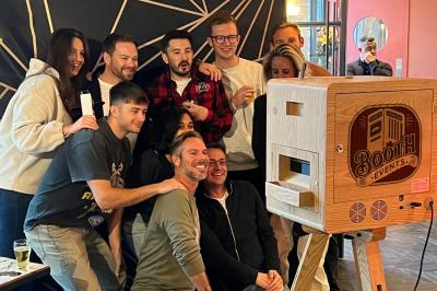 Logo illustré représentant une cabine photo rétro avec l'inscription ’Booth Events’ sur un fond rayé rouge et beige.