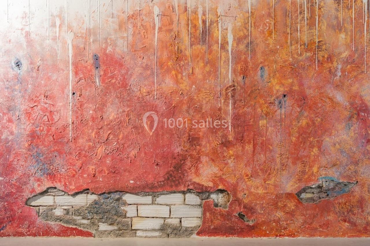 Mur texturé avec des teintes rouges et orangées, des coulures blanches et des zones où la brique est visible.