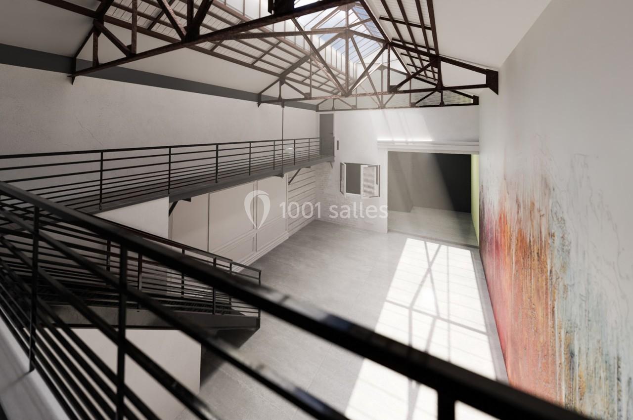 Intérieur d'un grand espace lumineux avec mezzanine, structure métallique apparente et mur décoré de motifs colorés.