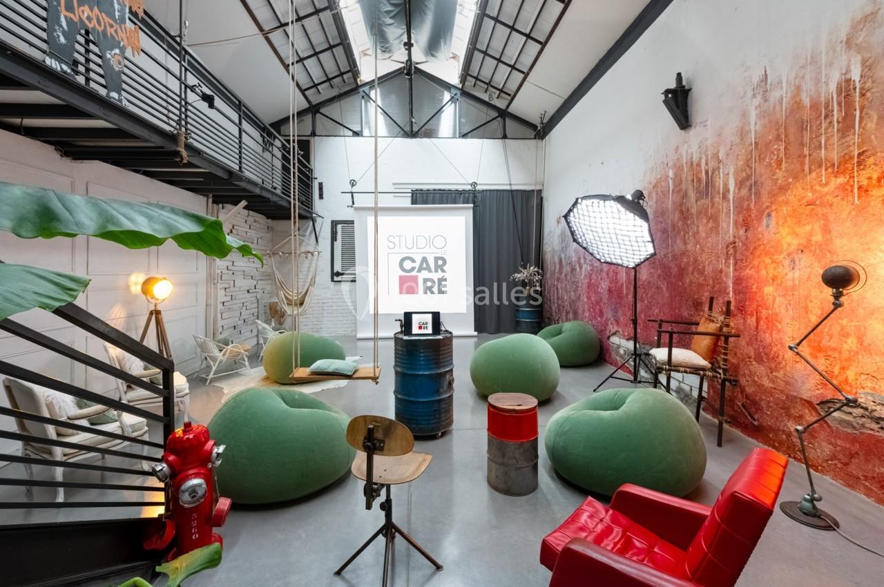 Salle aménagée avec des fauteuils, un écran de projection, des éclairages et une décoration industrielle colorée.