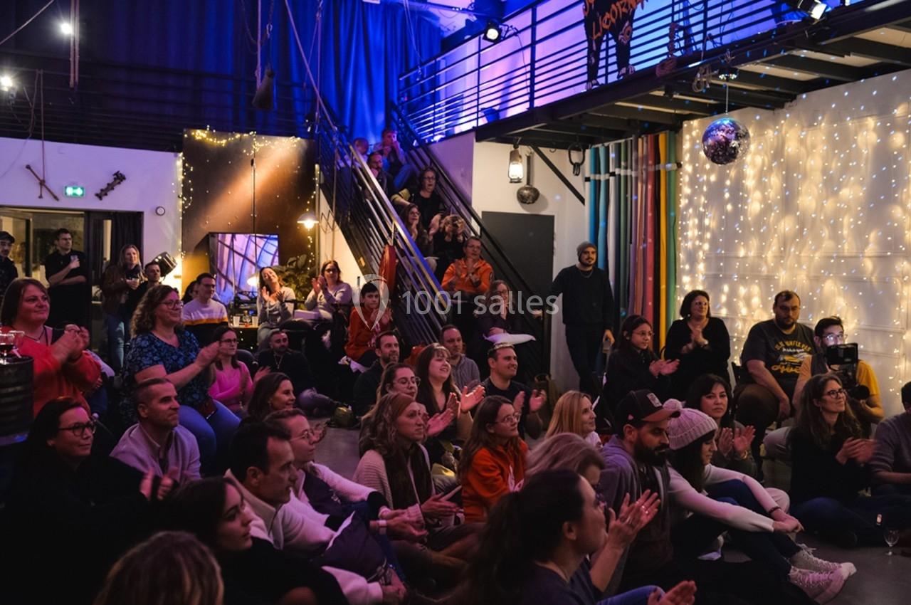 Un public assis applaudit dans une salle décorée de guirlandes lumineuses et d'une boule disco.