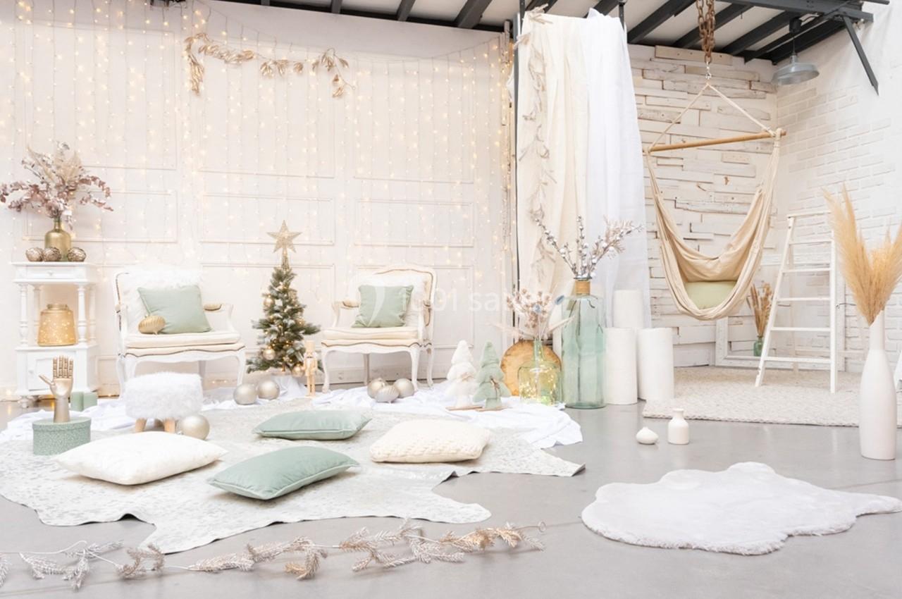 Décoration intérieure lumineuse avec sapin de Noël, fauteuils blancs, coussins pastel et guirlandes scintillantes.