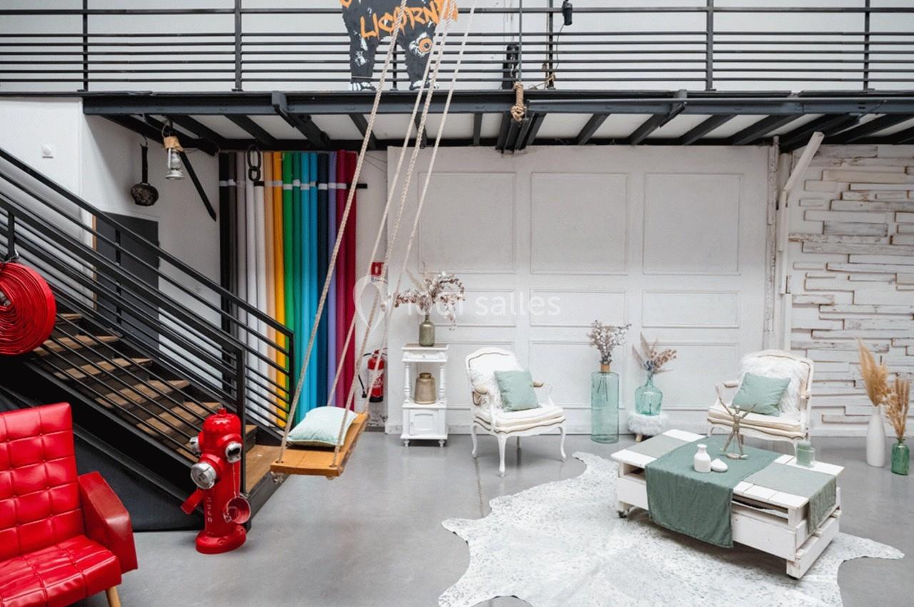 Espace lumineux avec mobilier vintage, balançoire intérieure, escalier noir et décorations colorées.