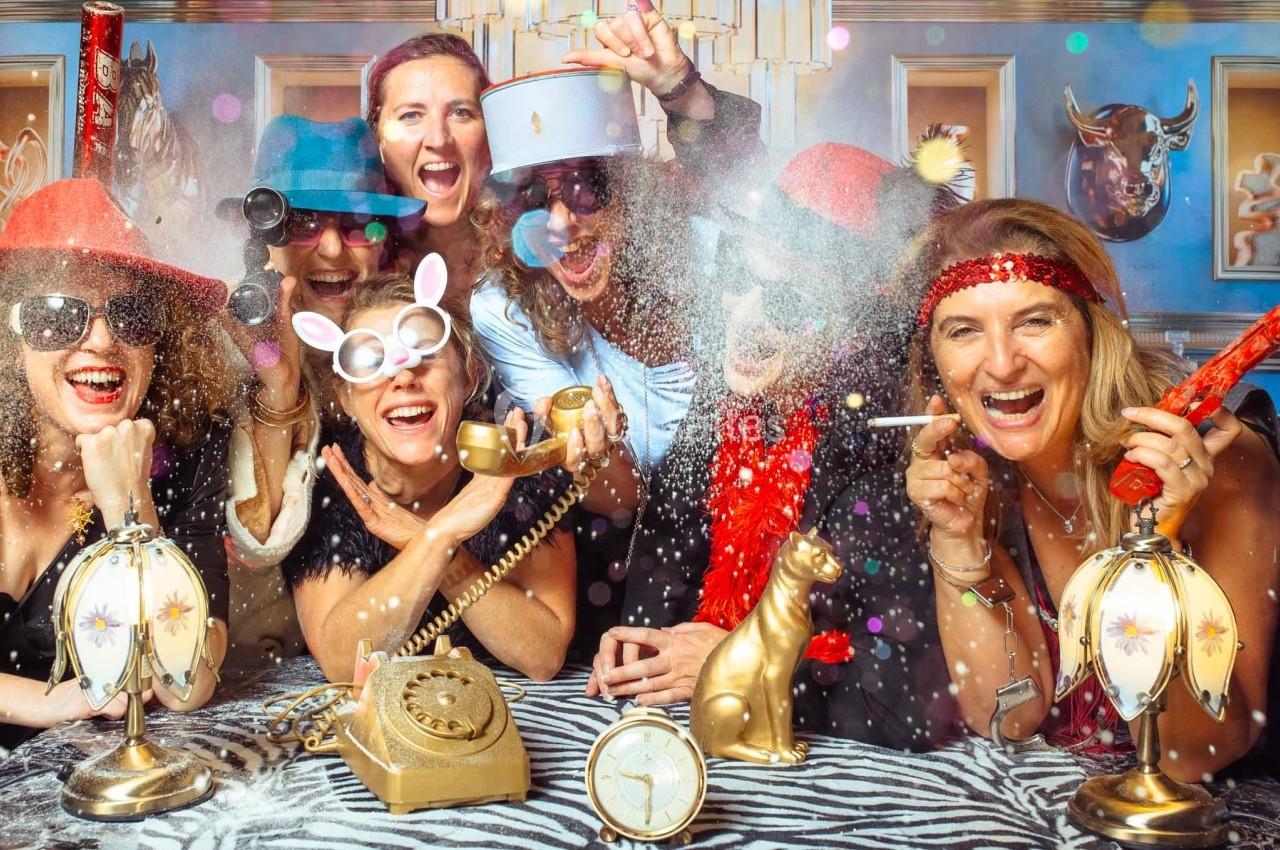 Un groupe de personnes déguisées s'amuse autour d'une table décorée avec des objets rétro et festifs.