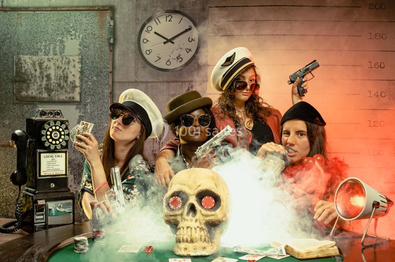 Quatre personnes déguisées autour d'une table de poker avec un crâne au centre, des cartes et des accessoires rétro.