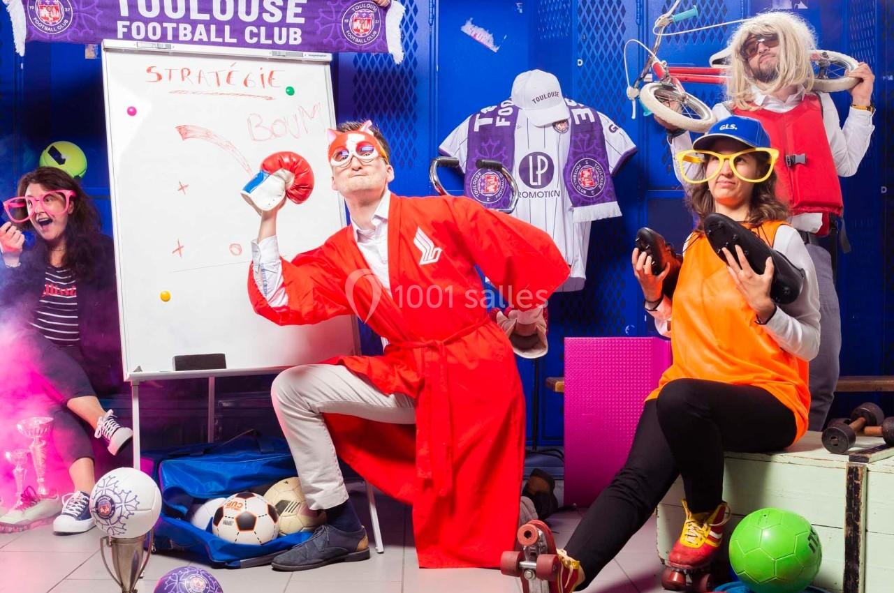 Des personnes déguisées dans un vestiaire de football, entourées d'accessoires sportifs et d'éléments humoristiques.