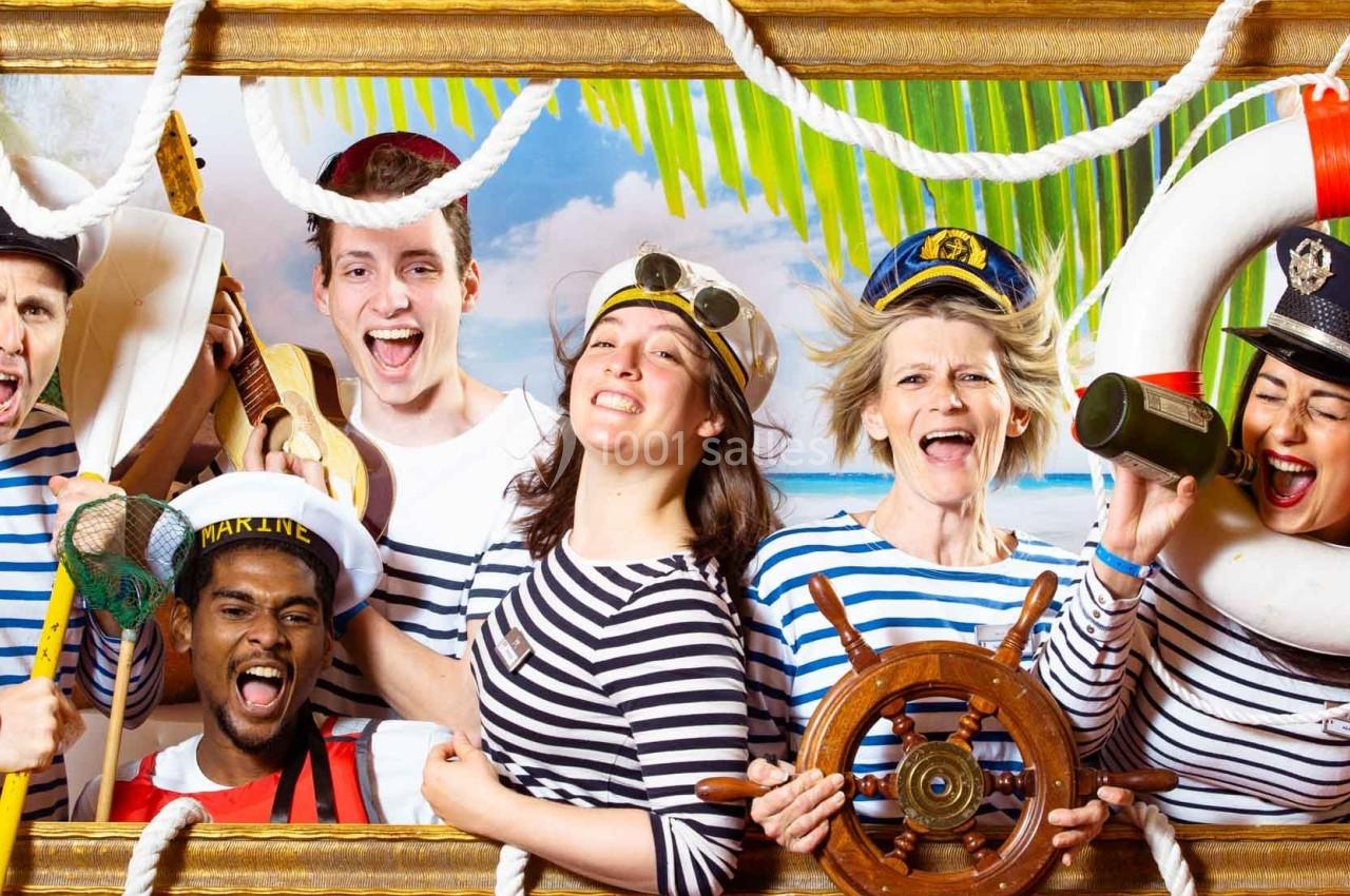 Des personnes déguisées en marins sourient et posent joyeusement avec des accessoires nautiques devant un décor tropical.