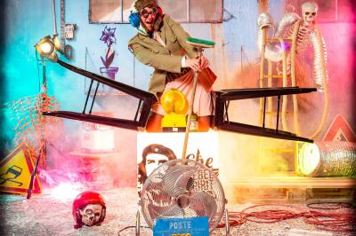 Miniature Studio le Carré #7 Femme portant des lunettes en forme de cœur jouant de la guitare électrique dans un décor rétro avec objets dorés.