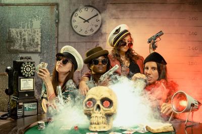 Miniature Studio le Carré #8 Femme portant des lunettes en forme de cœur jouant de la guitare électrique dans un décor rétro avec objets dorés.