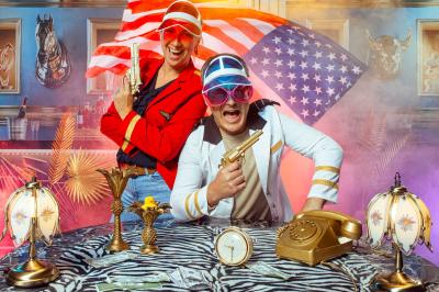 Miniature Studio le Carré #12 Femme portant des lunettes en forme de cœur jouant de la guitare électrique dans un décor rétro avec objets dorés.