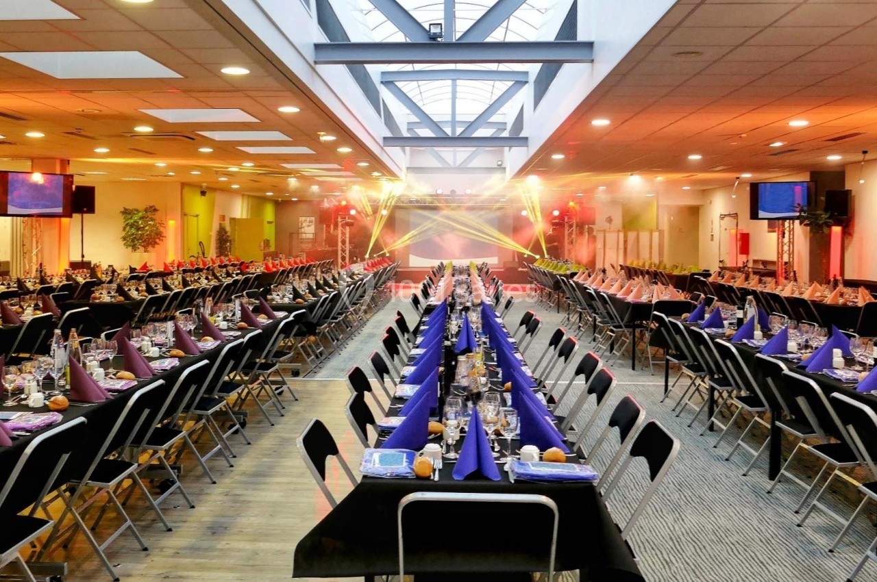 Salle de réception aménagée avec de longues tables dressées, éclairage coloré et ambiance festive.