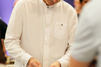 Serviettes blanches roulées posées sur un lit avec des oreillers et des draps blancs en arrière-plan.