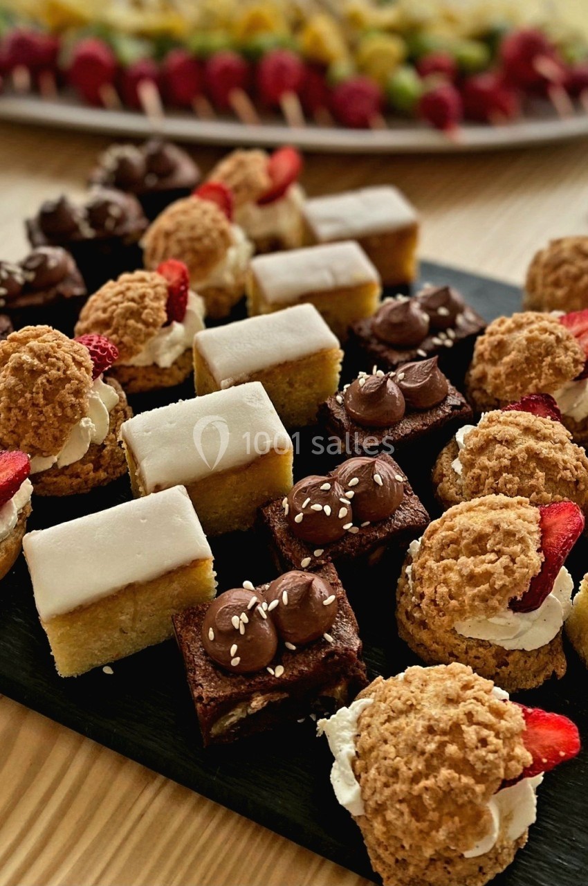 Plateau de mignardises variées comprenant choux garnis, gâteaux glacés et brownies décorés, présenté sur une table en bois.