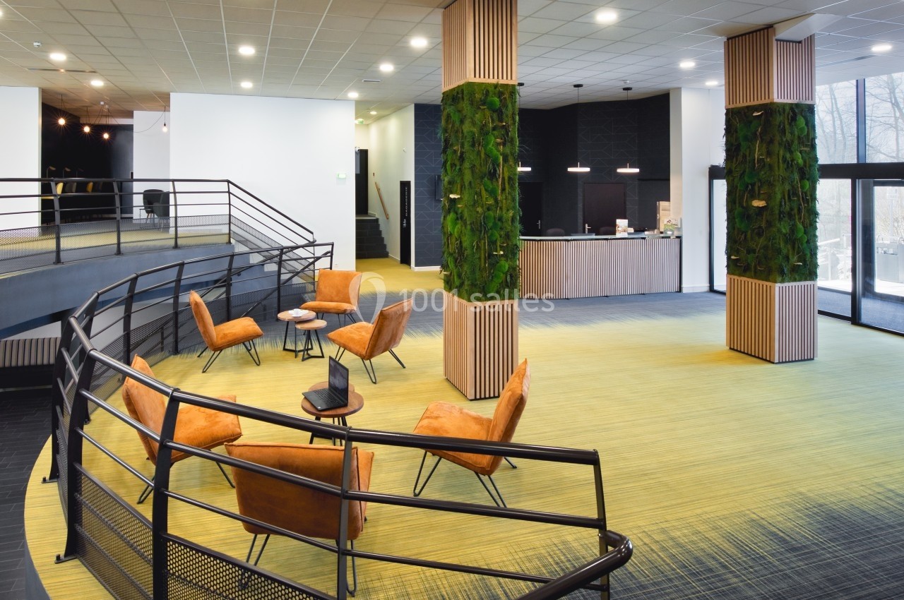 Espace intérieur moderne avec fauteuils orange, murs végétalisés, comptoir d'accueil et grande baie vitrée.