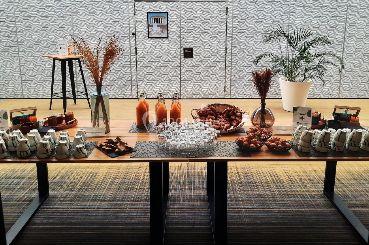 Buffet composé de boissons, viennoiseries, pots de yaourt et décorations sur une table en bois dans une salle lumineuse.