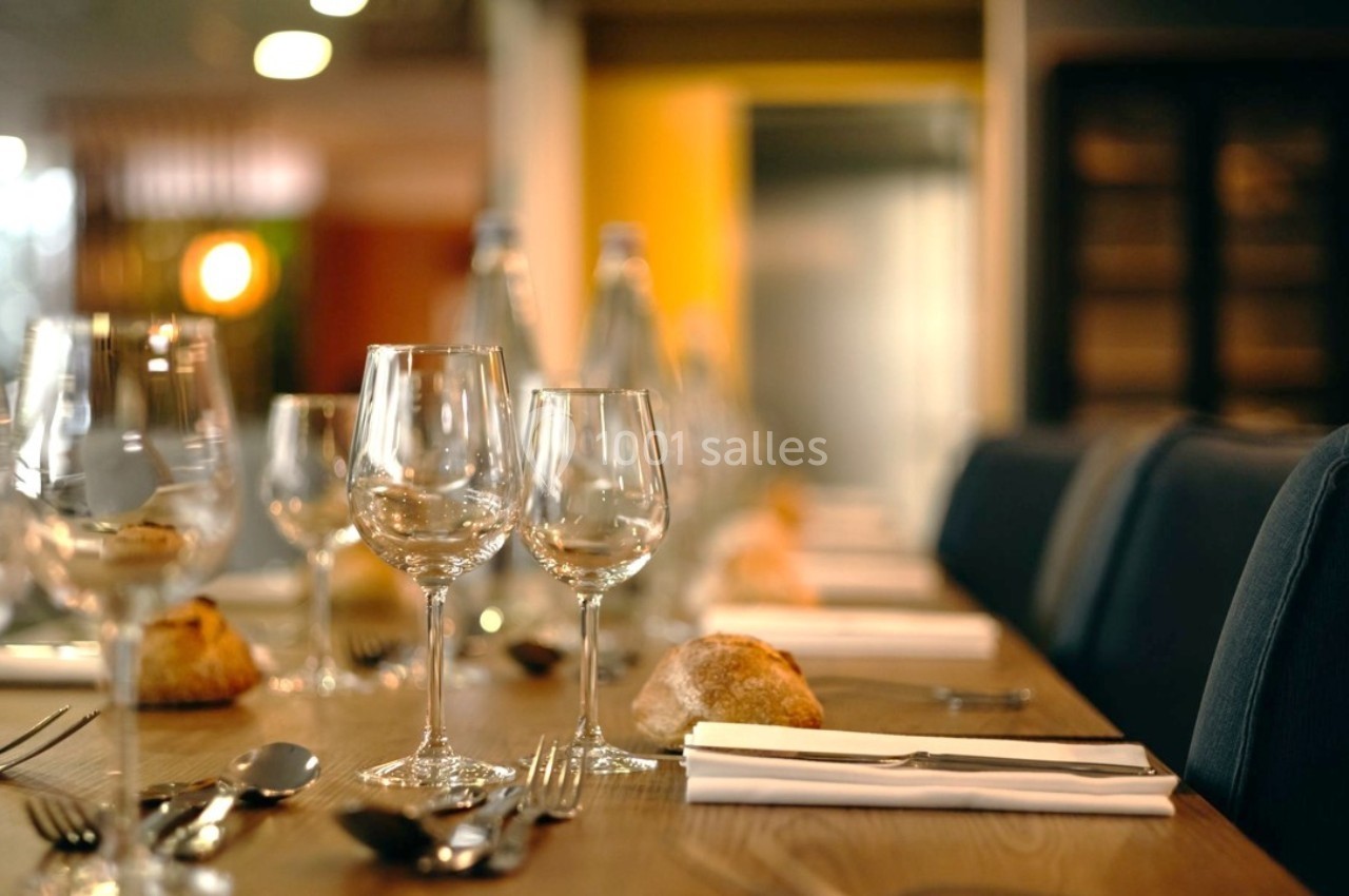 Table dressée avec des verres à vin, couverts, serviettes et petits pains dans un cadre chaleureux.