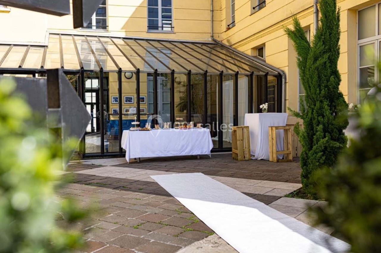 Cour intérieure avec verrière, tables dressées pour un événement et chemin blanc menant à une zone aménagée.