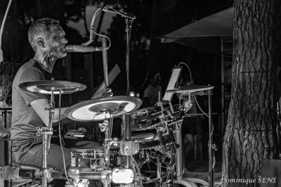 Miniature DJ Milizac (Finistère) - Florian Rion #5 Homme en chemise noire, lunettes de soleil, fumant un cigare, tenant un verre devant un bar rempli de bouteilles.