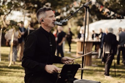 Miniature DJ Milizac (Finistère) - Florian Rion #4 Homme en chemise noire, lunettes de soleil, fumant un cigare, tenant un verre devant un bar rempli de bouteilles.