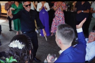 Miniature DJ Milizac (Finistère) - Florian Rion #3 Homme en chemise noire, lunettes de soleil, fumant un cigare, tenant un verre devant un bar rempli de bouteilles.