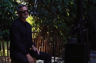 Miniature DJ Milizac (Finistère) - Florian Rion #19 Homme en chemise noire, lunettes de soleil, fumant un cigare, tenant un verre devant un bar rempli de bouteilles.