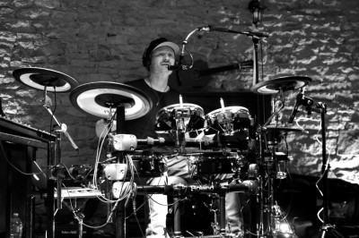 Miniature DJ Milizac (Finistère) - Florian Rion #2 Homme en chemise noire, lunettes de soleil, fumant un cigare, tenant un verre devant un bar rempli de bouteilles.