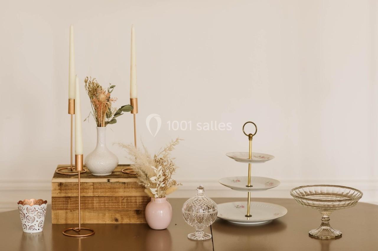 Décoration de table avec chandeliers dorés, vases fleuris, présentoir à étages et plats en verre sur une surface en bois.