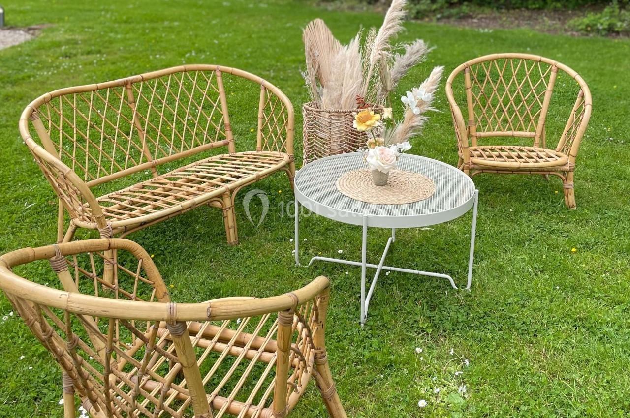 Salon de jardin en rotin avec table basse ronde, décoré de fleurs séchées, installé sur une pelouse verte.