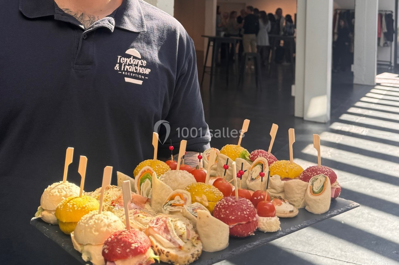 Plateau de bouchées apéritives variées, présenté par une personne en uniforme dans un espace lumineux.