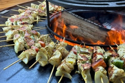 Miniature Traiteur Leers (Nord) - Tendance et Fraicheur Traiteur #17 Brochettes de viande et légumes grillant sur un barbecue en plein air, avec une fontaine et un jardin en arrière-plan.